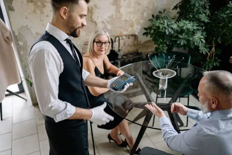A server holds a handheld payment terminal out to a couple at a restaurant table